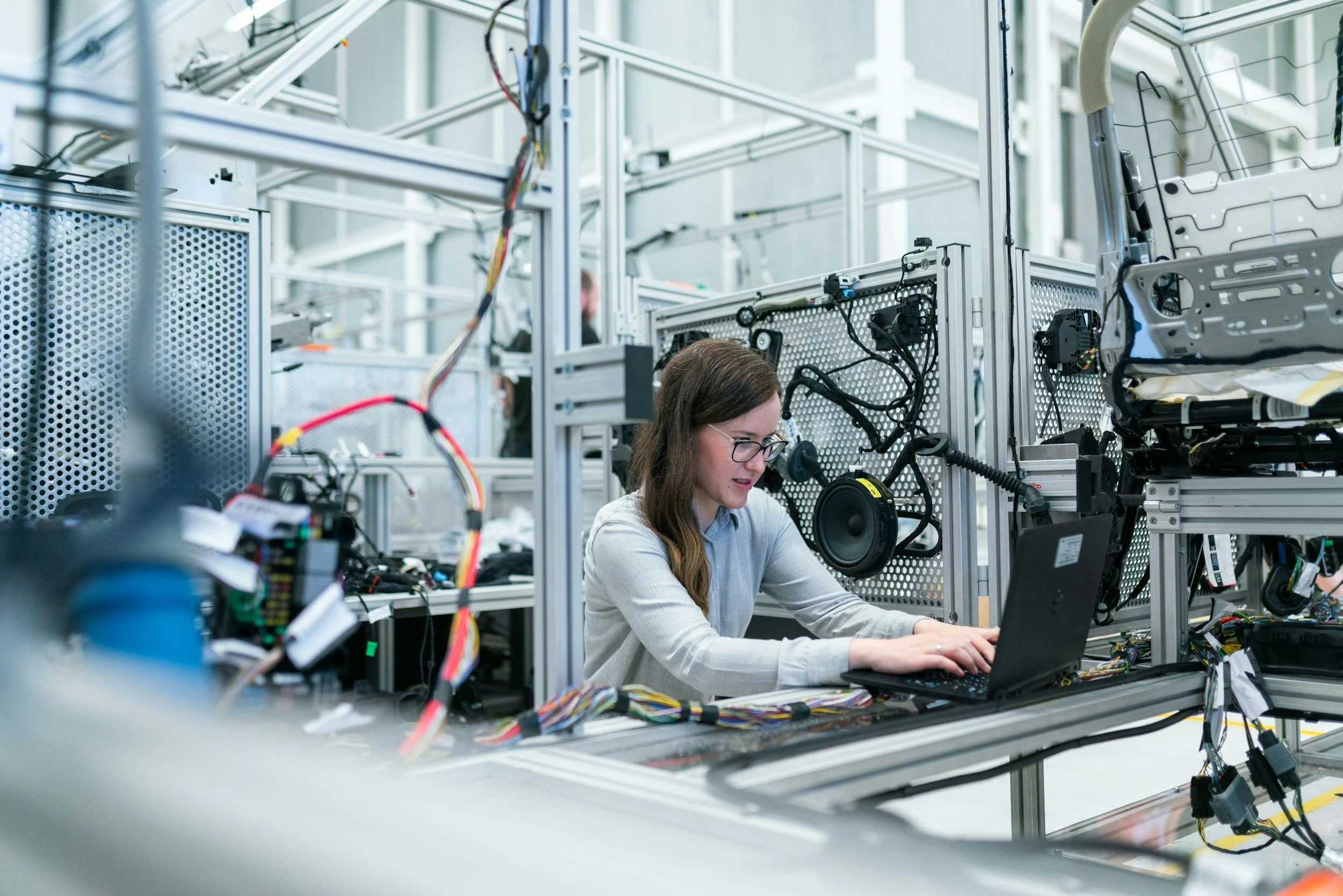A woman sitting at a laptop surrounded by wires and parts